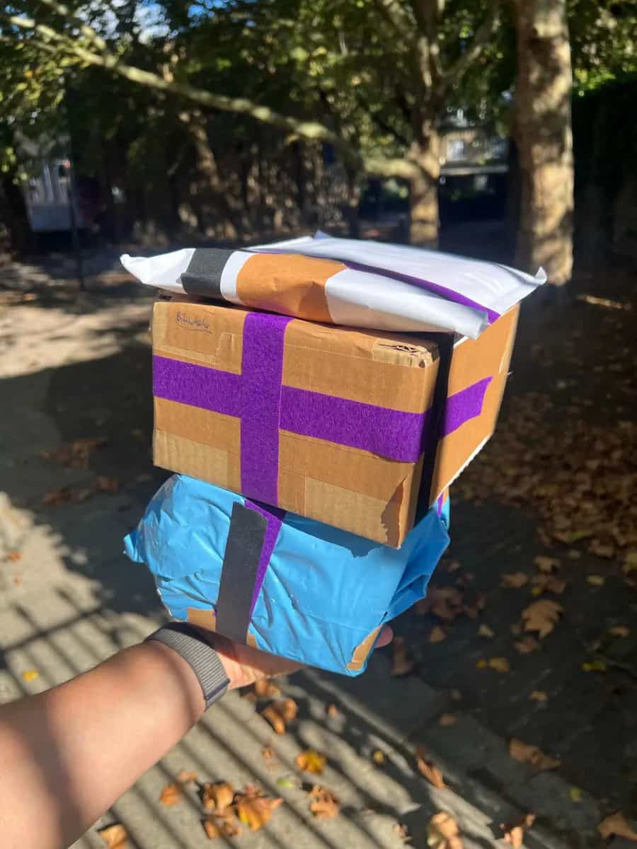 A hand holding a stack of three taped book parcels outside under the trees