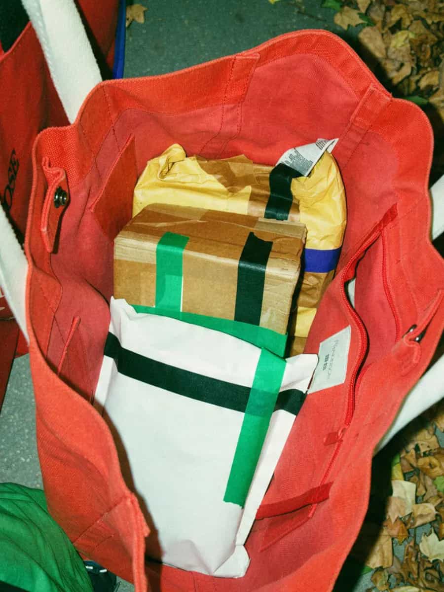 A red tote bag full of taped parcels on an autumn pavement covered in fallen leaves